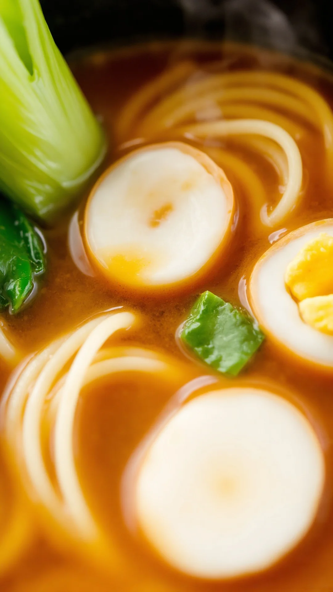 Close-up macro shot of pak choi ramen with fluffy noodles swirling in golden broth, soft boiled egg in center, fresh green ve
