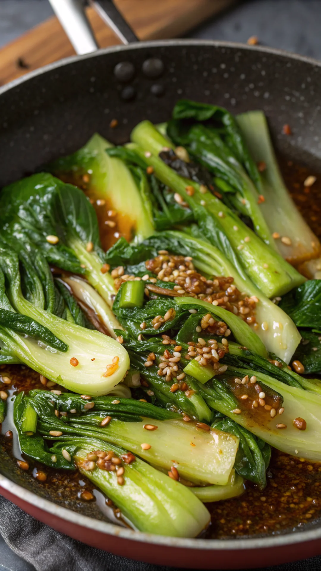 Close-up overhead shot of pak choi pieces in pan with savory sauce, glistening vegetables, sesame oil sheen, freshly cooked,